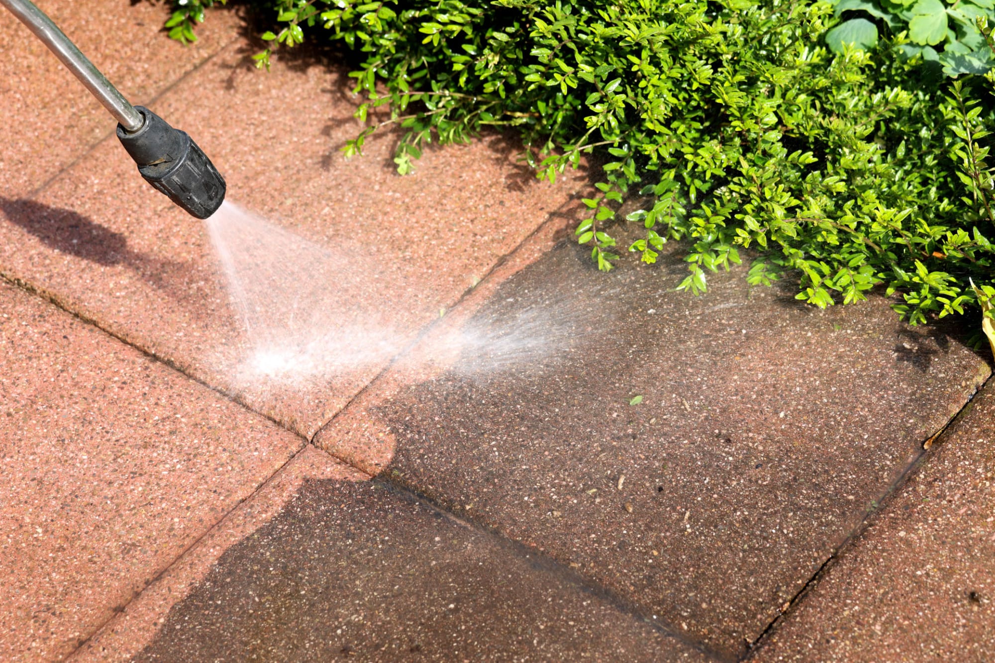 Pressure washing a paved walkway beside landscaping